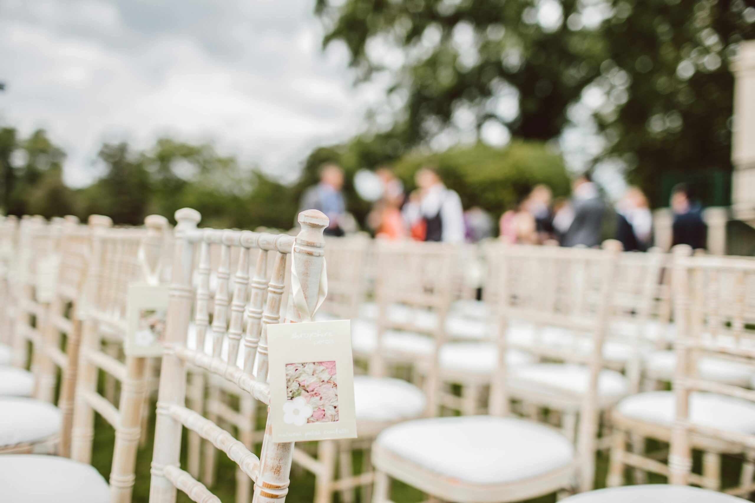 Elegant outdoor wedding setup with wooden chairs and blurred background.