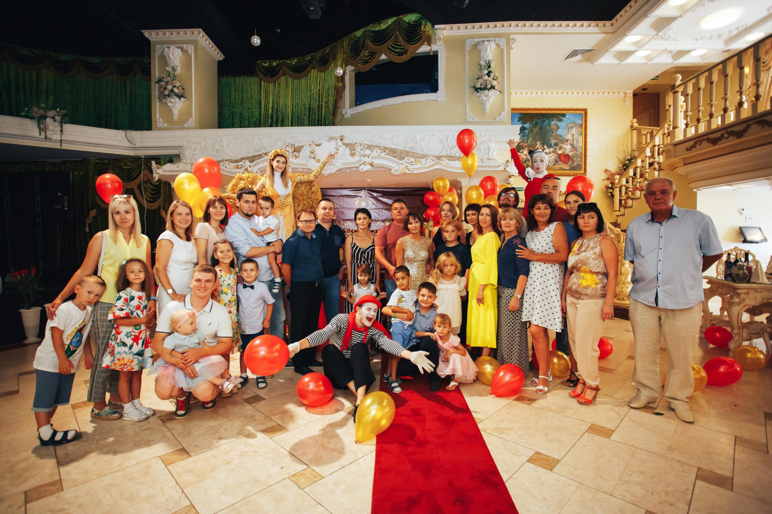 Group of people enjoying a festive indoor party with clowns and colorful balloons.