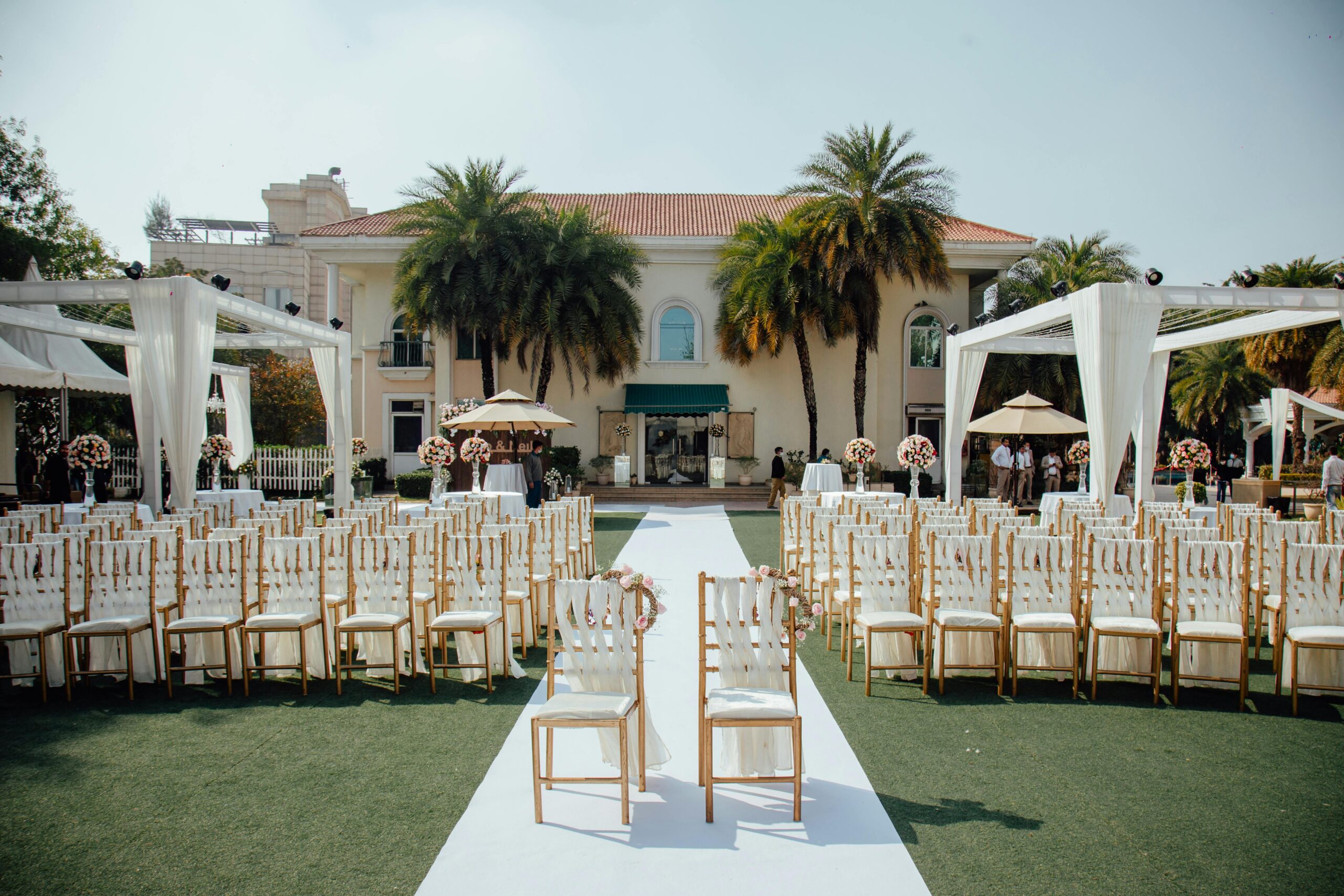 Beautiful outdoor wedding ceremony setup with rows of decorated chairs facing a luxurious villa.